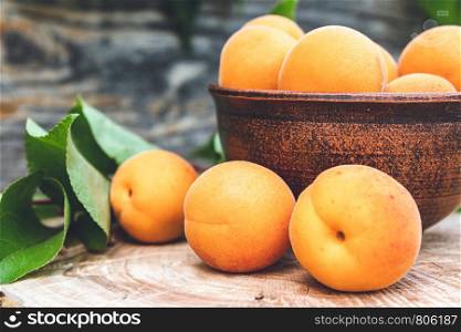 Delicious ripe apricots in a bowl next to green leaves on a wooden table. Close-up.. Delicious ripe apricots in a bowl next to green leaves on a wooden table.
