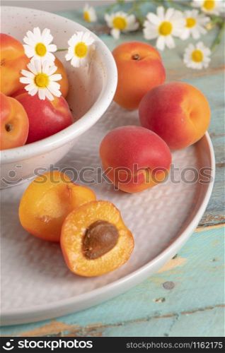 Delicious ripe apricots in a bowl on the wooden table. Close-up with apricots and daisy flowers