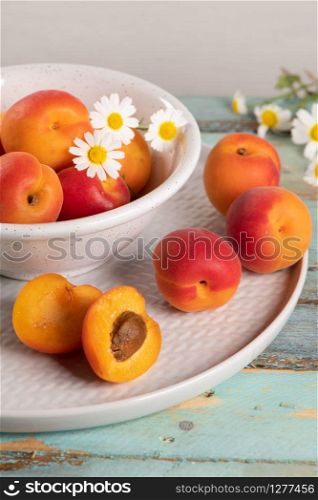 Delicious ripe apricots in a bowl on the wooden table. Close-up with apricots and daisy flowers