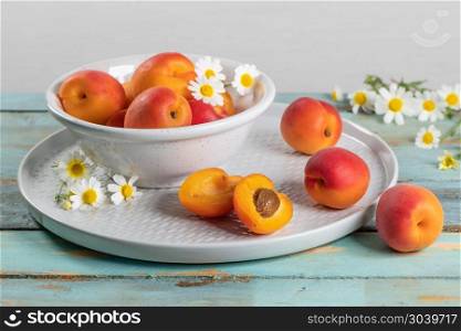 Delicious ripe apricots in a bowl on the wooden table. Close-up . Delicious ripe apricots in a bowl on the wooden table. Close-up with apricots and daisy flowers