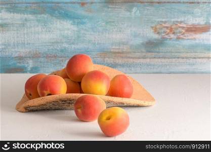 Delicious ripe orange apricots in a cork plate on white table on light blue wall background. Fresh juicy fruits. Bio vegetarian food village concept.