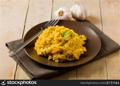 delicious risotto with saffron on wooden table with garlic and napkin