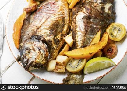 Delicious roasted fish carp with fruits on the plate. Prepared fried fish in fruit.