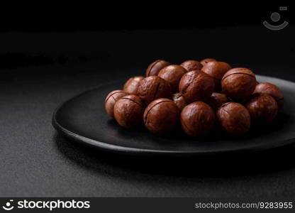 Delicious roasted macadamia nuts in shell on a dark textured concrete background. Vegetarian food