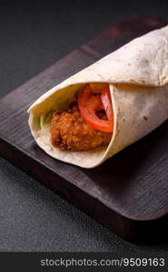 Delicious roll with chicken nuggets, tomatoes, lettuce and sauces with salt and spices on a dark concrete background