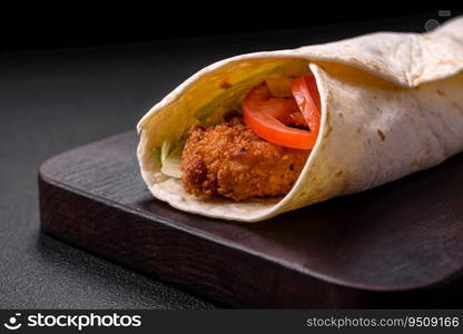 Delicious roll with chicken nuggets, tomatoes, lettuce and sauces with salt and spices on a dark concrete background