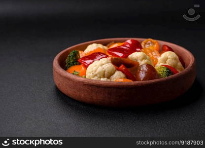 Delicious salad of fresh cherry tomatoes, sweet peppers, broccoli and cauliflower with salt and spices on a dark concrete background