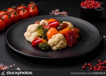Delicious salad of fresh cherry tomatoes, sweet peppers, broccoli and cauliflower with salt and spices on a dark concrete background