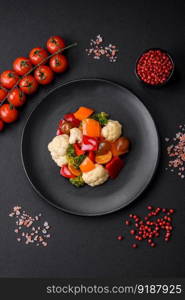 Delicious salad of fresh cherry tomatoes, sweet peppers, broccoli and cauliflower with salt and spices on a dark concrete background