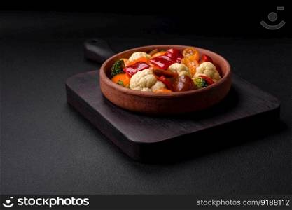 Delicious salad of fresh cherry tomatoes, sweet peppers, broccoli and cauliflower with salt and spices on a dark concrete background