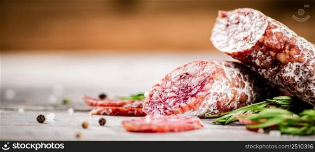 Delicious salami sausage with rosemary. On a wooden background. High quality photo. Delicious salami sausage with rosemary.