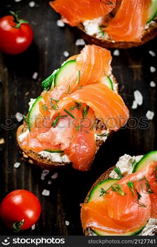 Delicious salmon sandwich on the table. On a wooden background. Top view. High quality photo. Delicious salmon sandwich on the table.