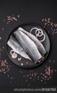 Delicious salted herring fillet in oil on a black ceramic plate on a dark concrete background