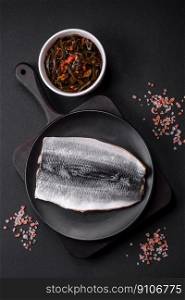 Delicious salted herring fillet in oil on a black ceramic plate on a dark concrete background