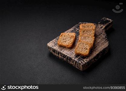 Delicious salted rectangular wheat croutons with salt and spices on a dark concrete background