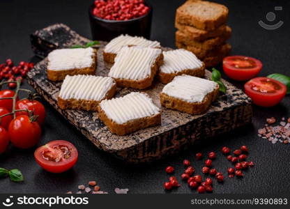 Delicious salty rectangular wheat croutons with cream cheese, tomatoes, salt and spices on a dark concrete background