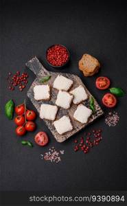 Delicious salty rectangular wheat croutons with cream cheese, tomatoes, salt and spices on a dark concrete background