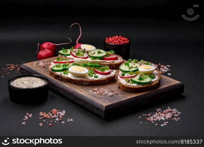 Delicious sandwich or bruschetta with cream cheese radish and green onions on a dark concrete background