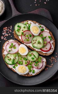 Delicious sandwich or bruschetta with cream cheese radish and green onions on a dark concrete background