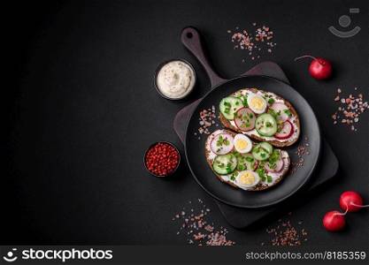 Delicious sandwich or bruschetta with cream cheese radish and green onions on a dark concrete background
