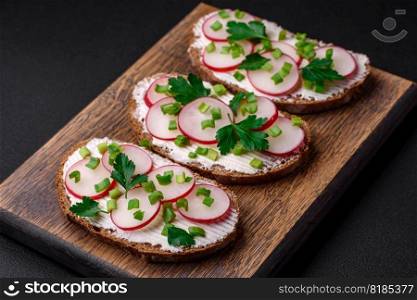Delicious sandwich or bruschetta with cream cheese radish and green onions on a dark concrete background