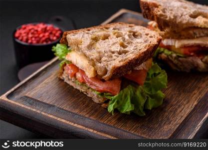 Delicious sandwich with crispy toast, chicken, tomatoes and lettuce on a dark concrete background
