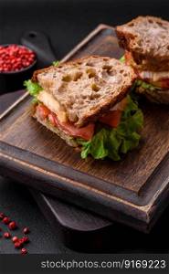 Delicious sandwich with crispy toast, chicken, tomatoes and lettuce on a dark concrete background