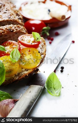 Delicious sandwich with slices of tomatoes and basil on white marble background