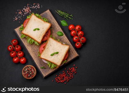 Delicious sandwich with toast, ham, tomatoes, cheese and lettuce with salt, spices and herbs on a dark concrete background