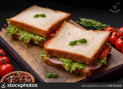 Delicious sandwich with toast, ham, tomatoes, cheese and lettuce with salt, spices and herbs on a dark concrete background