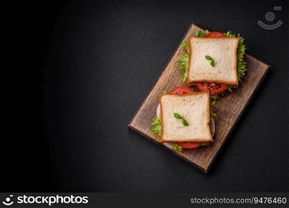 Delicious sandwich with toast, ham, tomatoes, cheese and lettuce with salt, spices and herbs on a dark concrete background