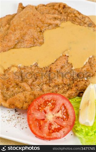 Delicious Schnitzel with lemon, tomato, lettuce and sauce.