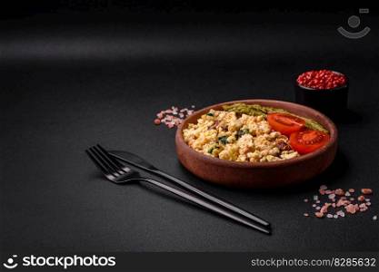 Delicious scramble with salmon, sun-dried tomatoes, spinach, spices and herbs on a dark background
