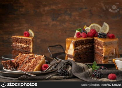 Delicious semi-naked chocolate cake with caramel topping and decorated with blackberries and raspberries. Dark background