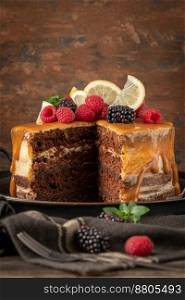 Delicious semi-naked chocolate cake with caramel topping and decorated with blackberries and raspberries. Dark background