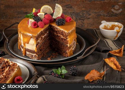 Delicious semi-naked chocolate cake with caramel topping and decorated with blackberries and raspberries. Dark background