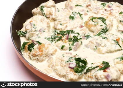 Delicious small meatballs with spinach in a creamy sauce in the frying pan. High quality photo. Delicious small meatballs with spinach in a creamy sauce in the frying pan