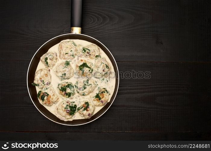 Delicious small meatballs with spinach in a creamy sauce in the frying pan. High quality photo. Delicious small meatballs with spinach in a creamy sauce in the frying pan