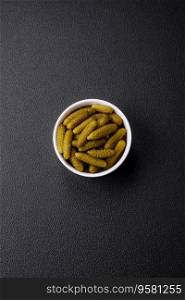 Delicious small pickled cucumbers gherkins with onions, mustard, salt and spices on a dark concrete background