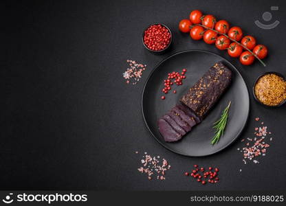 Delicious smoked Armenian basturma with spices and herbs sliced on a dark concrete background