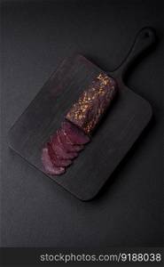 Delicious smoked Armenian basturma with spices and herbs sliced on a dark concrete background