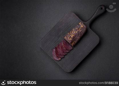 Delicious smoked Armenian basturma with spices and herbs sliced on a dark concrete background