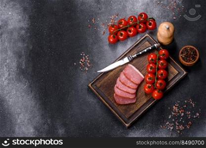 Delicious smoked meat cut with slices on a wooden cutting board against a dark grey concrete background. Delicious smoked meat cut with slices on a wooden cutting board