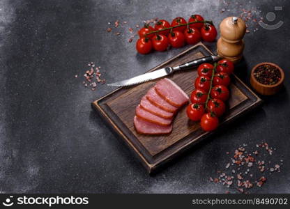 Delicious smoked meat cut with slices on a wooden cutting board against a dark grey concrete background. Delicious smoked meat cut with slices on a wooden cutting board