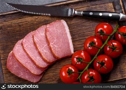 Delicious smoked meat cut with slices on a wooden cutting board against a dark grey concrete background. Delicious smoked meat cut with slices on a wooden cutting board