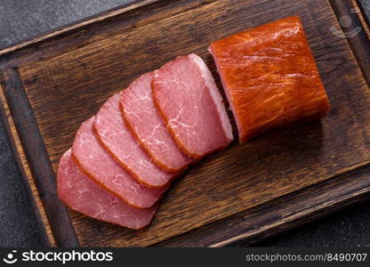 Delicious smoked meat cut with slices on a wooden cutting board against a dark grey concrete background. Delicious smoked meat cut with slices on a wooden cutting board