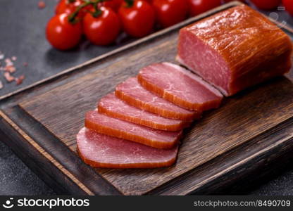 Delicious smoked meat cut with slices on a wooden cutting board against a dark grey concrete background. Delicious smoked meat cut with slices on a wooden cutting board