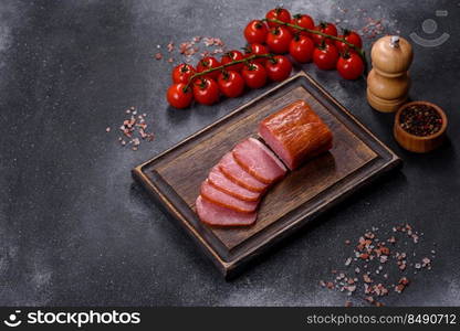 Delicious smoked meat cut with slices on a wooden cutting board against a dark grey concrete background. Delicious smoked meat cut with slices on a wooden cutting board