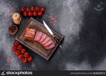 Delicious smoked meat cut with slices on a wooden cutting board against a dark grey concrete background. Delicious smoked meat cut with slices on a wooden cutting board