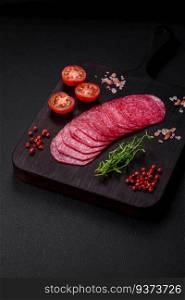 Delicious smoked salami sausage with salt, spices and herbs cut into slices on a dark concrete background